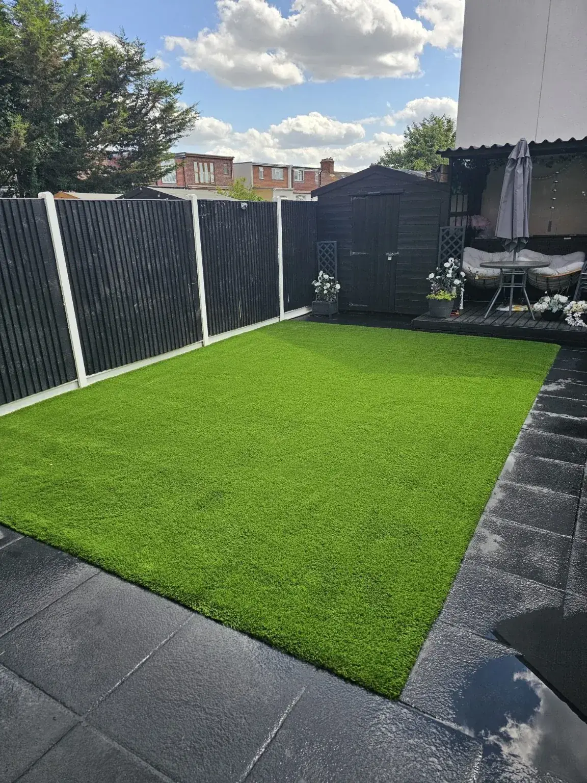 After installation: green artificial lawn bordered by existing paving and fencing