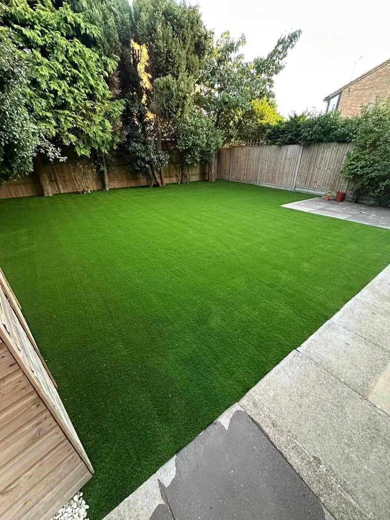 Completed artificial lawn bordered by mature trees, timber fencing and a paved patio
