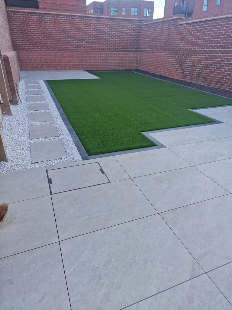 Completed artificial lawn in a brick-walled courtyard, with grey paving and a gravel stepping-stone path